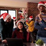 multiethnic-team-coworkers-using-laptop-christmas-working-project-office-decorated-with-festive-ornaments-xmas-tree-people-with-santa-hat-doing-teamwork-holiday_482257-47171